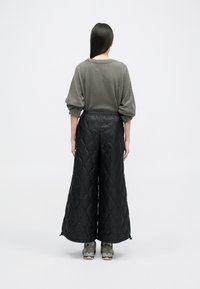 Juodi pakloti plataus kirpimo kelnes su elastinga juosmens linija, derinamos su pilkos spalvos per didelio dydžio megztiniu. Avalynėje yra pilkos spalvos tekstūruoti sportiniai bateliai.