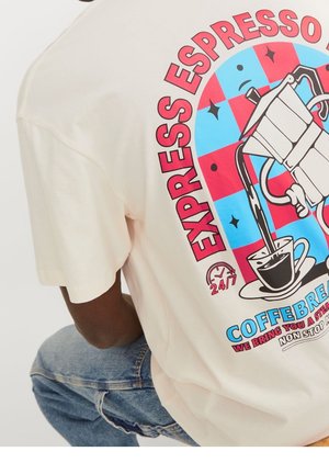 Person wearing a beige T-shirt with a graphic of a moka pot pouring coffee into a cup, text includes "EXPRESSO," "COFFEBREAK," and "24/7."