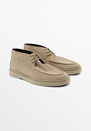 Beige ruskind ankelstøvler med rund tå, minimal syning og gummisål. Har snørebånd for sikker fastgørelse. Flad hældesign.