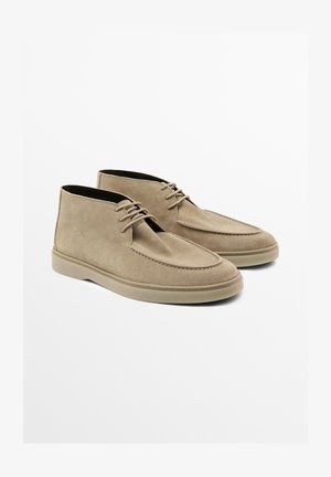 Stivaletti alla caviglia in suede beige con punta rotonda, cuciture minime e suola in gomma. Presentano lacci per una chiusura sicura. Design con tacco piatto.