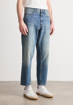 Lyse blå denimjeans med løs pasform, falmet ved knæene, lige ben, fem-lommet design, parret med hvide sneakers og grå sokker.