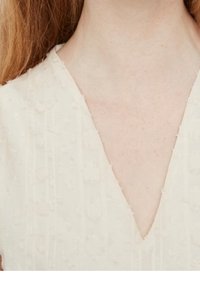 Cremefarbenes Kleid mit einem V-Ausschnitt, strukturiertem Stoff mit erhöhten Blumenmustern und subtiler Rippung.
