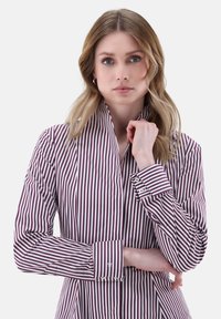 Camicia a righe bordeaux e bianca con colletto alto e polsini abbottonati, caratterizzata da un tessuto morbido e una vestibilità su misura.