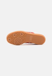 Sula på en vit och röd Adidas-sneaker som visar en texturerad gummisula med cirkulära och vågiga greppmönster.