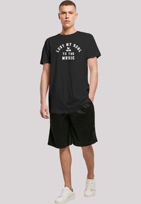 Black cotton t-shirt with the text "LOST MY SOUL TO THE MUSIC" in white. Worn with black shorts and white sneakers. Simple design, relaxed fit.