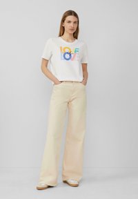 T-shirt blanc avec un graphique coloré "L'AMOUR est L'AMOUR". Assorti à un pantalon large beige clair et des chaussures décontractées beiges. Design simple et confortable.