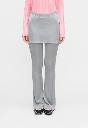 Szare prążkowane spodnie z dopasowaną szarą mini spódnicą na wierzchu, zestawione z różową bluzką z długim rękawem. Obuwie ma zaokrąglone noski i ozdoby.