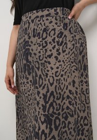 Leopardenmuster, beiger Stoffrock mit glatter Textur und hohem Taillenbund, ausgestattet mit seitlichen Taschen und einem fließenden Design.