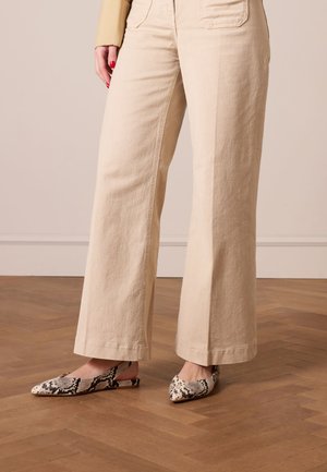 Beige wide-leg pants made of textured fabric, paired with pointed-toe slingback shoes in a black and white snake print.