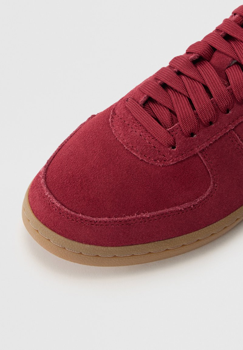 Baskets en daim rouge avec une texture lisse, bout rond et lacets ton sur ton. Elles présentent une semelle en caoutchouc gomme et des accents cousus pour plus de détails.