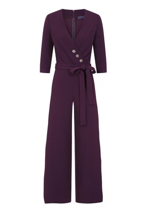 Fioletowy kombinezon z rękawami o długości trzech kwart, dekoltem w kształcie litery V, trzema dekoracyjnymi guzikami oraz pasującym paskiem z tkaniny. Szerokie, płaskie nogawki.