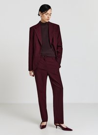 Costume bordeaux à fines rayures avec blazer ajusté et pantalon droit, accompagné d'un pull assorti cintré et de talons brillants à bouts pointus.