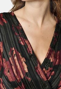 Haut noir à motifs floraux avec des plis verticaux ; présente des motifs de fleurs rouges et roses, un décolleté en V profond et un tissu texturé.