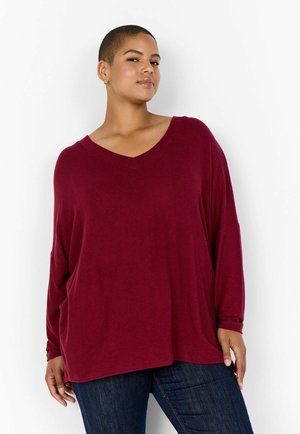 Haut bourgogne à manches longues avec un décolleté en V, coupe décontractée et épaules tombantes, fabriqué en tissu doux ; associé à un jean en denim foncé.