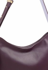 Paarse leren handtas met een zachte textuur, gebogen bovenrand en een dunne, verstelbare schouderriem met gouden hardware accenten.
