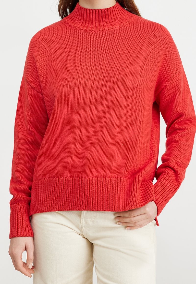 Rode gebreide trui met een hoge geribbelde kraag, lange mouwen en een geribbelde zoom. Gemaakt van zacht stof met een ontspannen pasvorm.