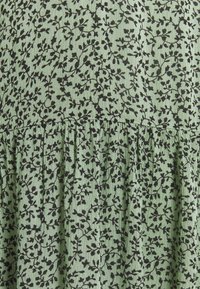 Zielona tkanina z czarnym kwiatowym wzorem. Posiada marszczony dół i teksturowaną powierzchnię. Wzór składa się z nakładających się gałęzi i liści.