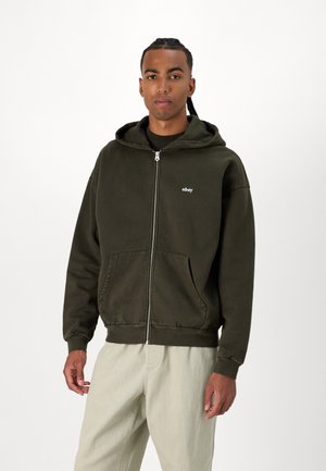 Olive green zip-up hoodie made of soft fabric, featuring a front pocket and a small white logo on the left chest. Simple design, relaxed fit.