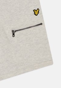 Lichtgrijze t-shirt met een geborduurd geel vogellogo en een zwarte ritszak aan de zijkant. Zacht, gestructureerd stof.