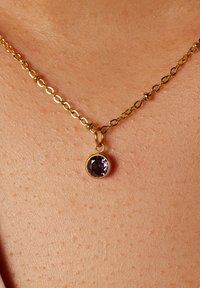Gouden ketting met een ovale schakelenontwerp, met een ronde paarse edelsteen hanger gezet in een gouden zetting.