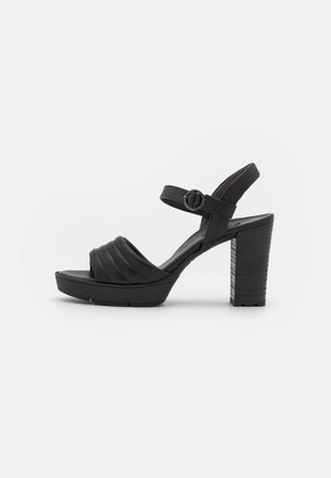 Sandalias negras de tacón con un tacón grueso, que cuentan con un diseño de tira acolchada y una correa ajustable en el tobillo, fabricadas en cuero suave.