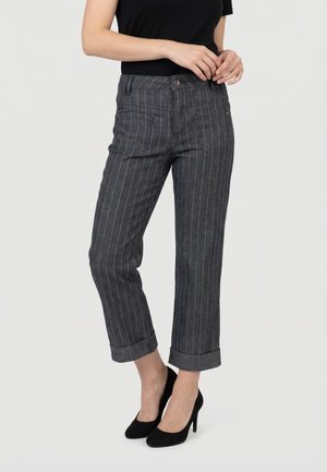 Donna che indossa pantaloni corti a righe sottili grigio scuro con orli risvoltati e tacchi alti neri, in piedi con le mani vicino alla vita.