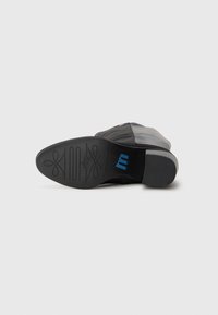 Black leather shoe with a smooth upper and a textured rubber sole featuring a blue logo and decorative pattern details.