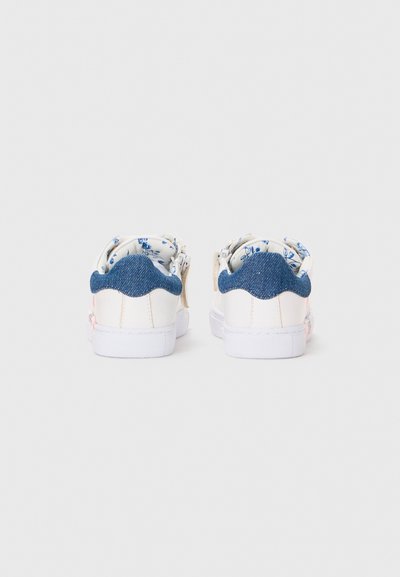 White sneakers with a denim heel, floral print lining, scalloped design at the back, and a textured rubber sole.