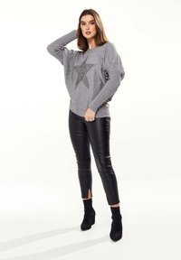 Gray sweater with a large star design, paired with glossy black leather pants featuring ankle slits, complemented by black heeled boots.