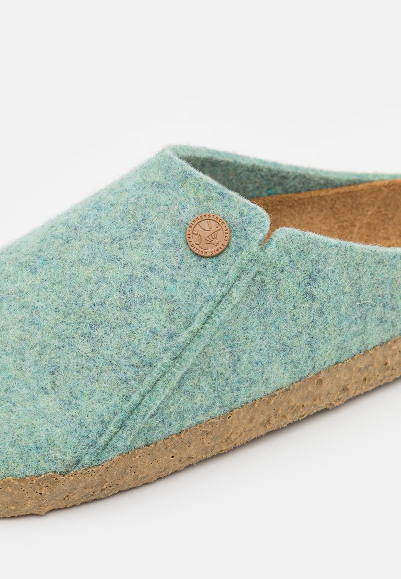 Chaussons en feutre vert avec une tige texturée et une semelle en liège marron. Présente une forme arrondie et un petit accent logo sur le côté.