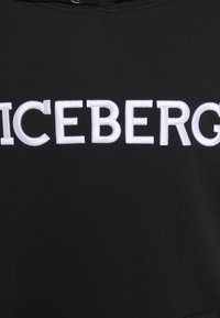 Sudadera negra con gran logotipo bordado en blanco "ICEBERG" en la parte delantera. El material parece suave y con una textura lisa.