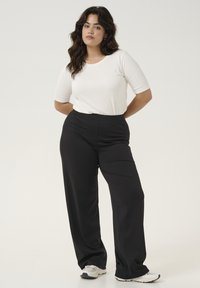 T-shirt ajusté blanc à manches courtes associé à un pantalon noir taille haute ; le modèle porte des baskets blanches et argentées.