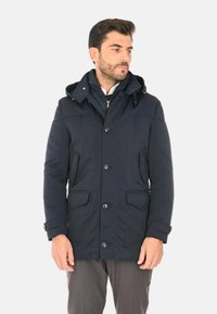 Parka imbottito blu navy con cappuccio staccabile, chiusura frontale con bottoni, due tasche laterali e una finitura liscia e texturizzata.