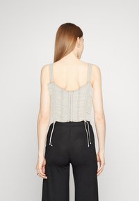 Ljusgrå kort topp med justerbara dragsko, rynkade detaljer och dragkedjestängning bak. Bärs med svarta högmidjade byxor.