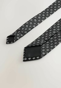 Fekete nyakkendő fehér hópehely mintával, sima anyagból készült. Az alja egyszínű fekete, és hegyes végű.