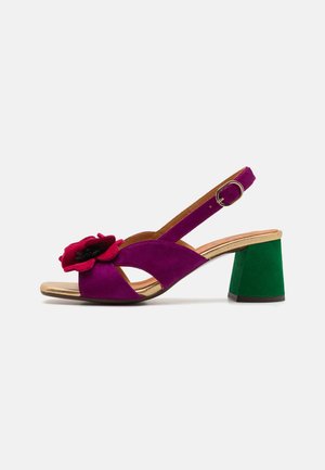 Lilla semsket sandal med en stor rød blomst detalj, åpen tå, slingback-design og en kontrasterende grønn blokkhelt. Gulvtonet fotbed.