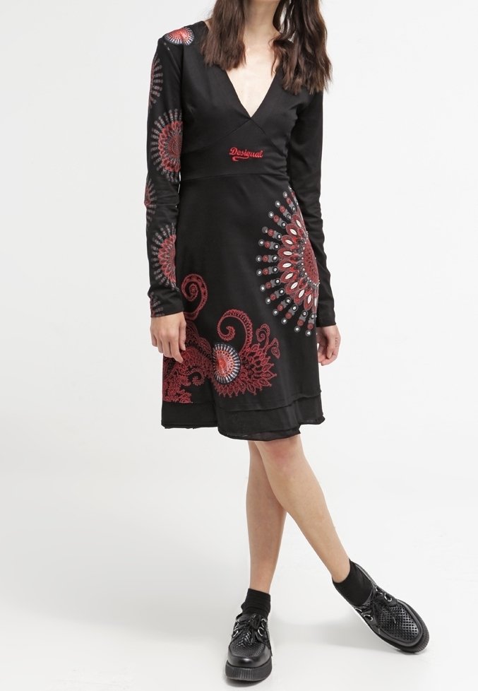 Femme portant une robe noire à manches longues avec des motifs circulaires rouges et blancs et des chaussures noires à semelles épaisses.