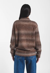 Pull rayé marron en tissu doux et duveteux avec une coupe décontractée. Comprend un col et des poignets côtelés, accompagné d'un jean bleu.