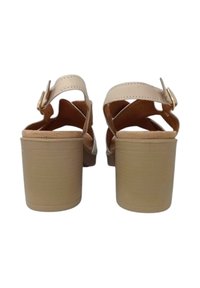 Sandali con tacco beige caratterizzati da un design a fascia incrociata e una fibbia regolabile. Il tacco a blocco è solido e rivestito in un materiale liscio.