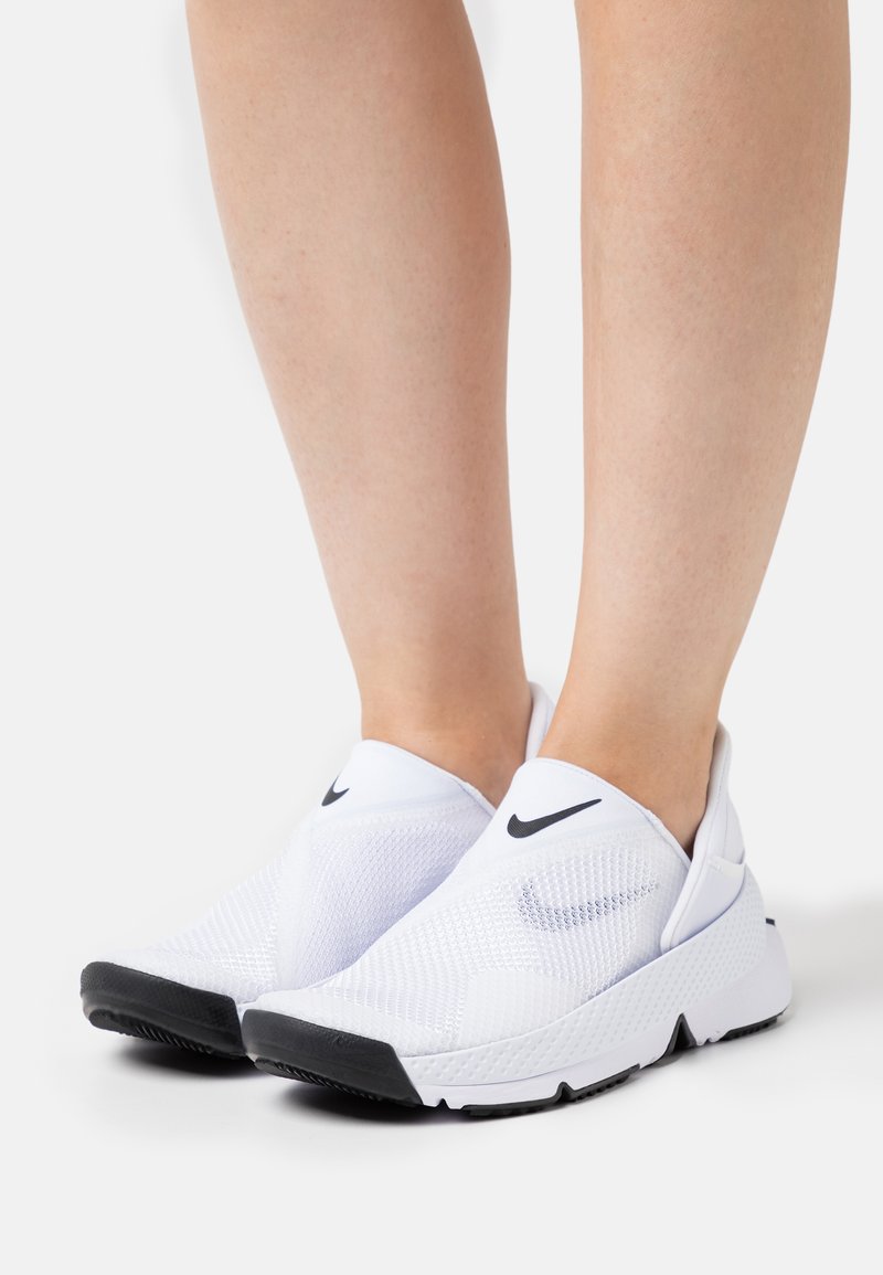 Zapatillas deportivas blancas tipo slip-on con parte superior de malla, que presentan un logo de Nike en negro, suela texturizada y un diseño aerodinámico.