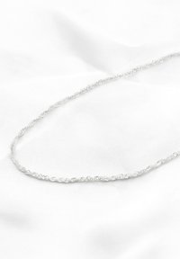 Sølv kædedyse med et snoet design, der har en glat overflade og et ensartet mønster, liggende på en hvid stofbaggrund.