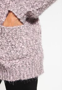 Chunky stickad tröja i lavendel med en strukturerad väv. Har en framficka och ribbad fåll. Mjuk, fluffig material och oversize passform.