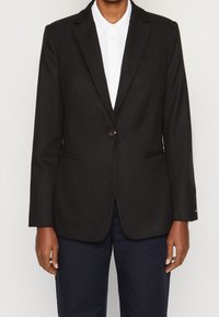 Svart skräddarsydd blazer i slätt tyg, med en enkel knappstängning, slim fit och diskret logodetalj på bröstfickan.
