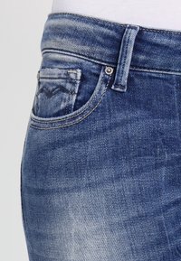 Mörkblå denimjeans med en lätt blekningseffekt, femficksdesign och en knappstängning med synliga sömnadsdetaljer.
