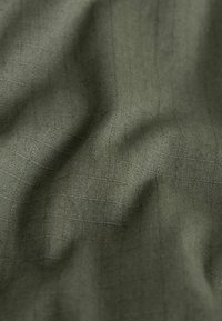 Gros plan sur un tissu vert olive avec une texture subtile de grille tissée et de doux plis créant des variations de lumière et d'ombre.