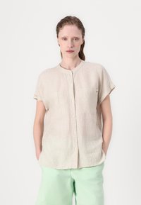 Camicia button-up beige chiaro a maniche corte, con sottili righe verticali e due tasche anteriori. Tessuto morbido e testurizzato.