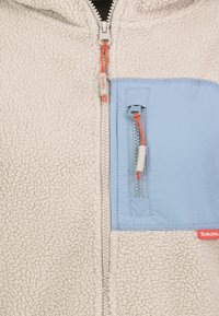 Fleecejack met off-white kleur en een blauw paneel; voorzien van een oranje ritslipje en zak. Gestructureerde stof met contrasterend glad detail.