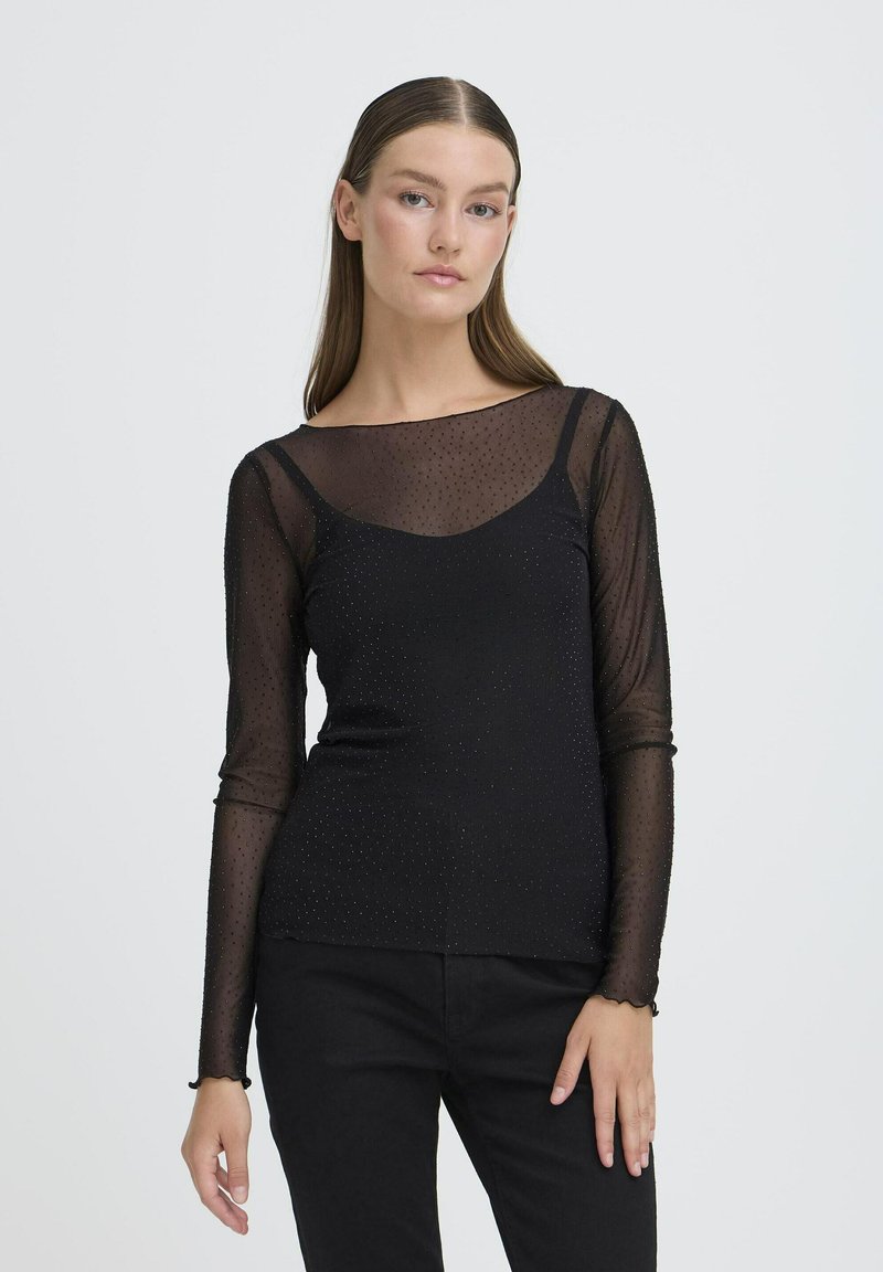 Maglietta nera a maniche lunghe con overlay trasparente a pois, scollatura a barca e sottogiacca aderente, arricchita da leggere ruches sui polsini.