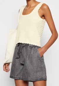 Débardeur en maille texturée beige clair avec des bords scallopés, associé à un short en denim gris foncé ample avec une taille à nouer et des poches latérales.