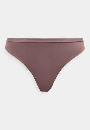 Brūnas bezšuvju bikini biksītes ar Calvin Klein logotipu uz vidukļa lentes, attēlotas pret vienkāršu gaišu fonu.